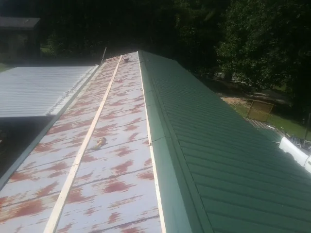 Old rusted panels beside newly installed green metal roofing — Wind Damage Roof Repair by Roofing Brothers in Seville