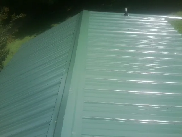 New green metal panels meeting at the ridge of a roof — Flat Roof Repair work by our crew in Seville