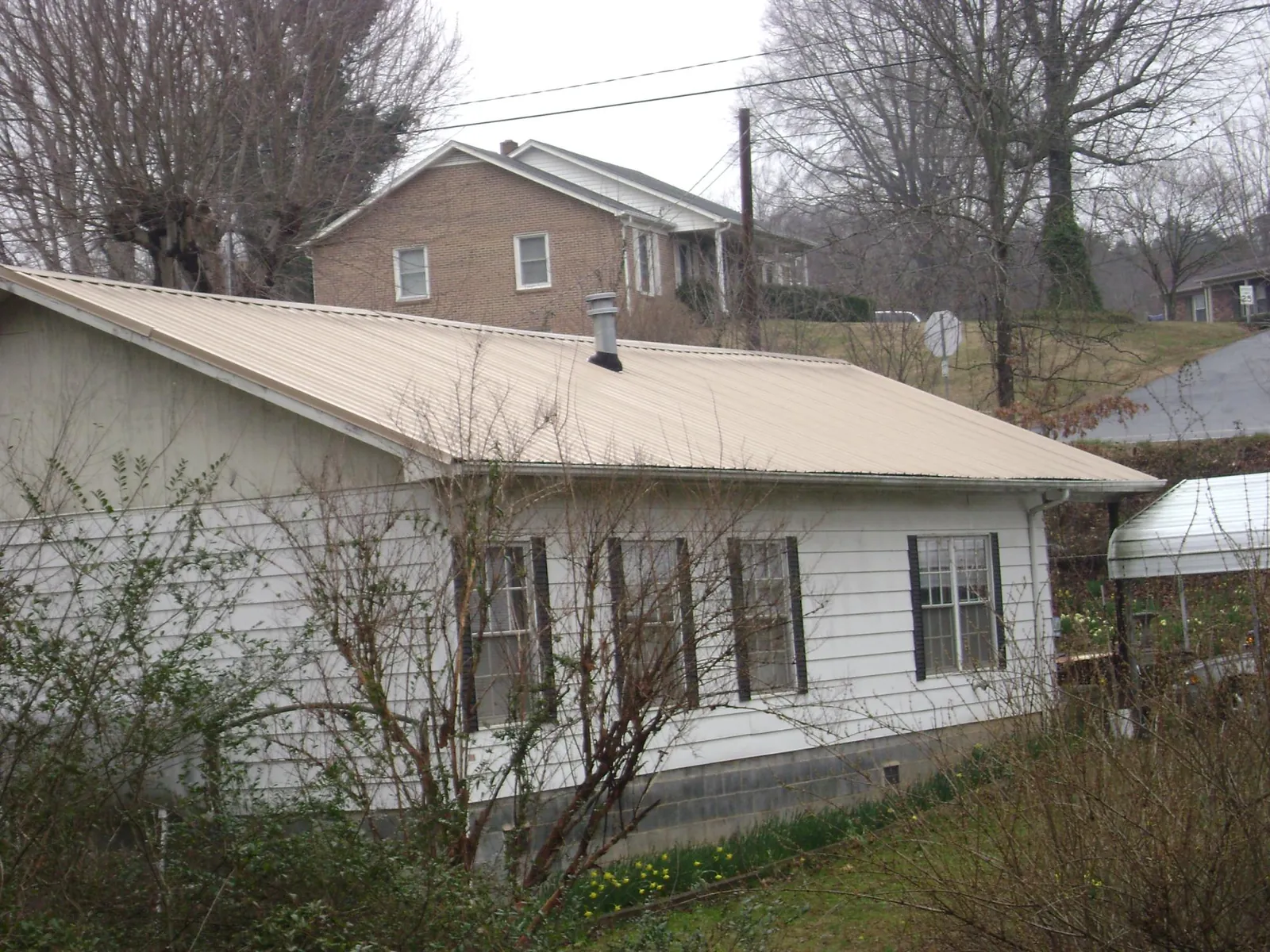 Tan metal roof on a white sided house set into a hillside — Commercial Roofing by Roofing Brothers in Seville