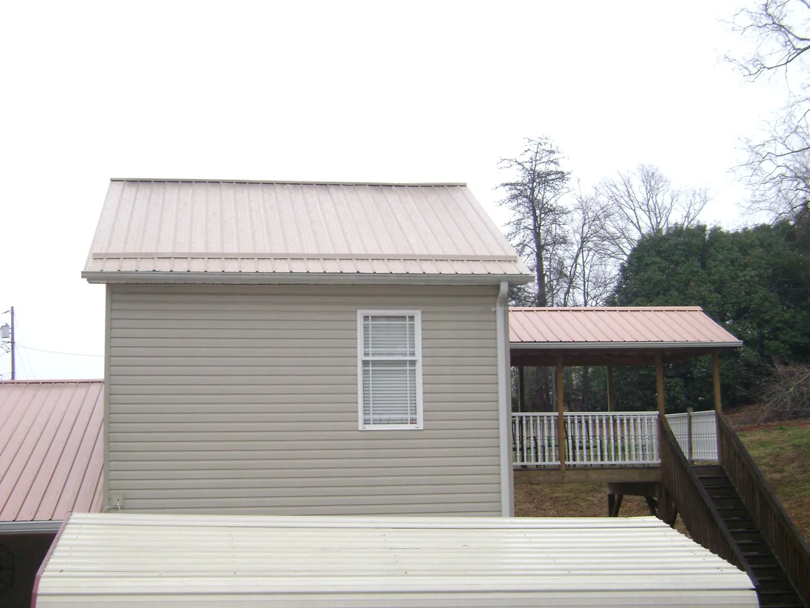 Tan metal roofs on a two story addition and attached porch, from a Roof Replacement job in Seville